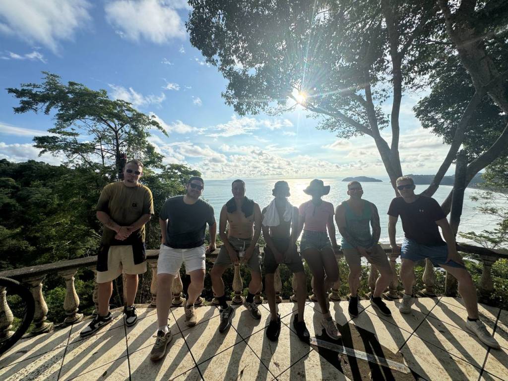 A bachelor party group posing for a photo on a scenic overlook overlooking the ocean and coastline of Jaco, Costa Rica.